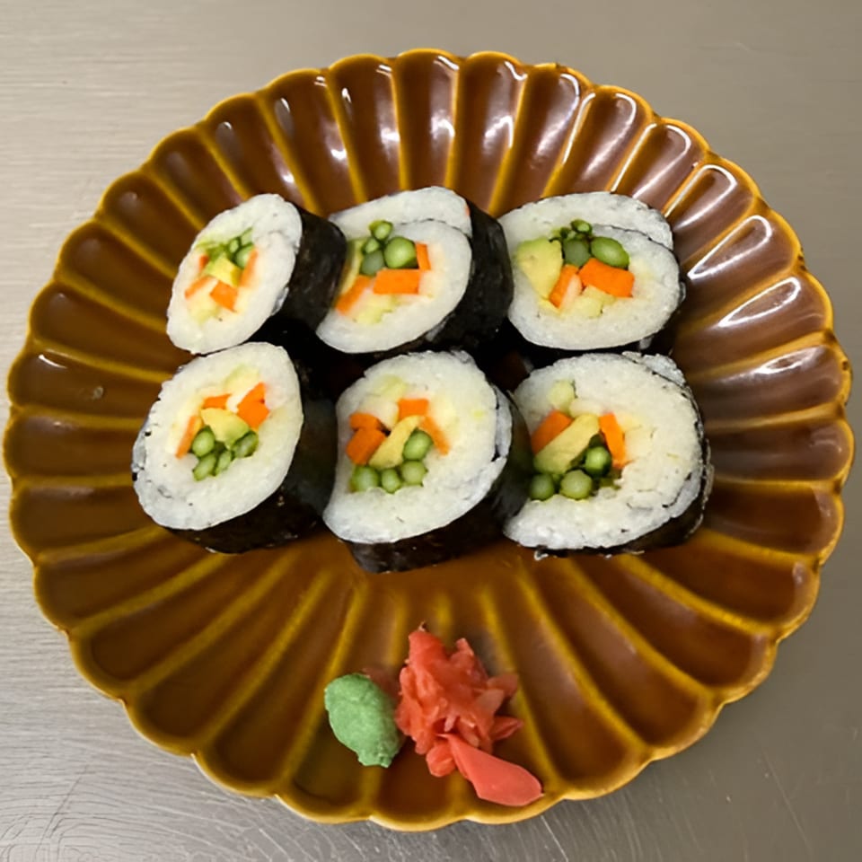 Six vegetable sushi rolls arranged on a scalloped brown plate with wasabi and pickled ginger.