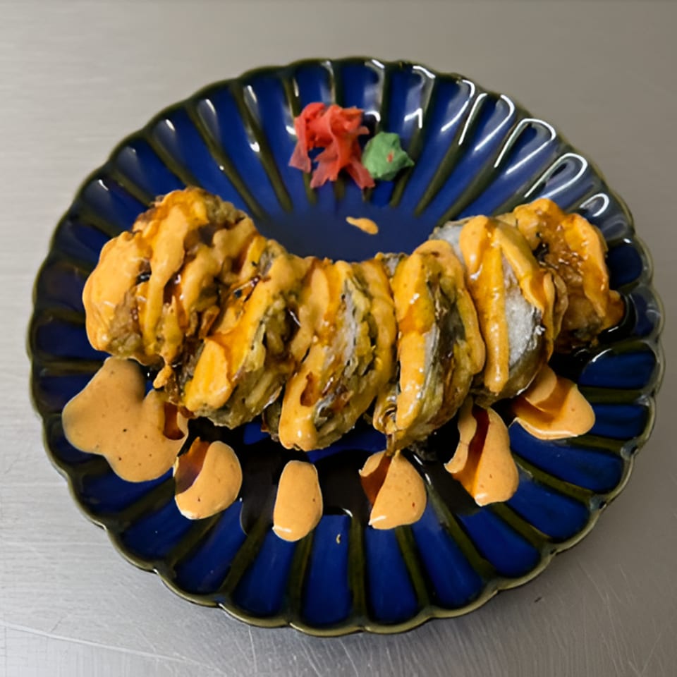 Grilled sliced seafood skewer drizzled with orange sauce on a blue plate, garnished with a red flower and green leaf.
