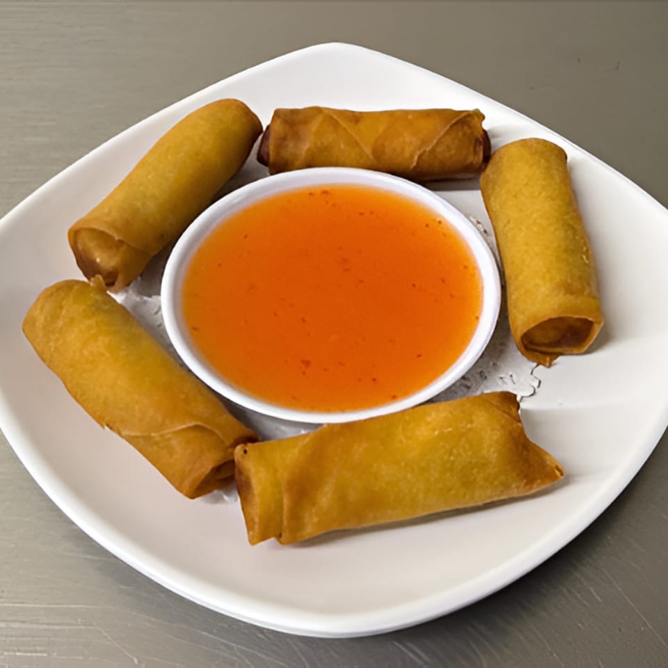 Five golden spring rolls arranged around a bowl of bright orange dipping sauce on a white plate.