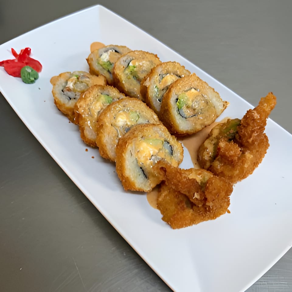 Crispy sushi rolls and fried shrimp arranged on a white rectangular plate with red and green garnish.