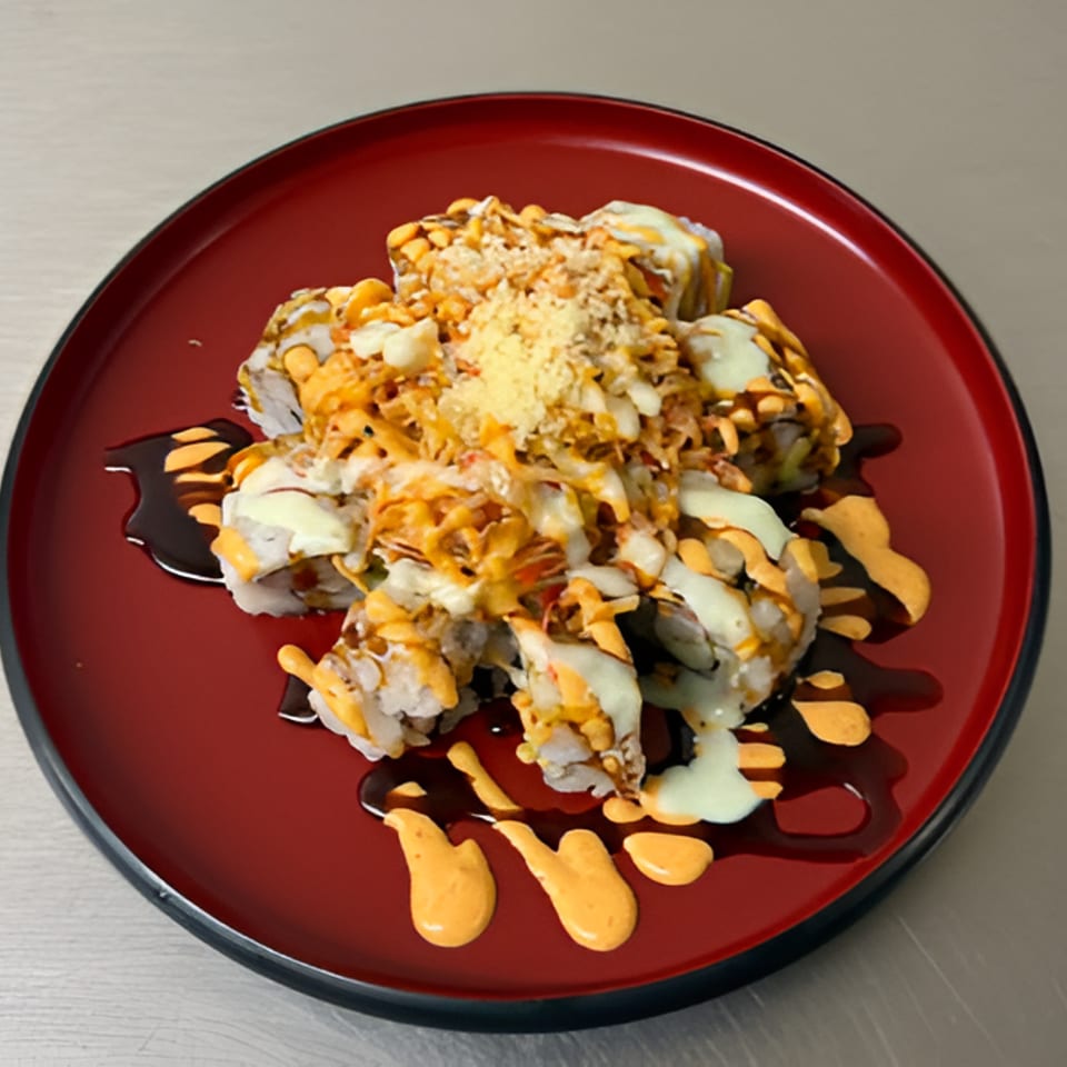 Sushi rolls topped with crunchy flakes and drizzled with creamy white and orange sauces on a red plate.