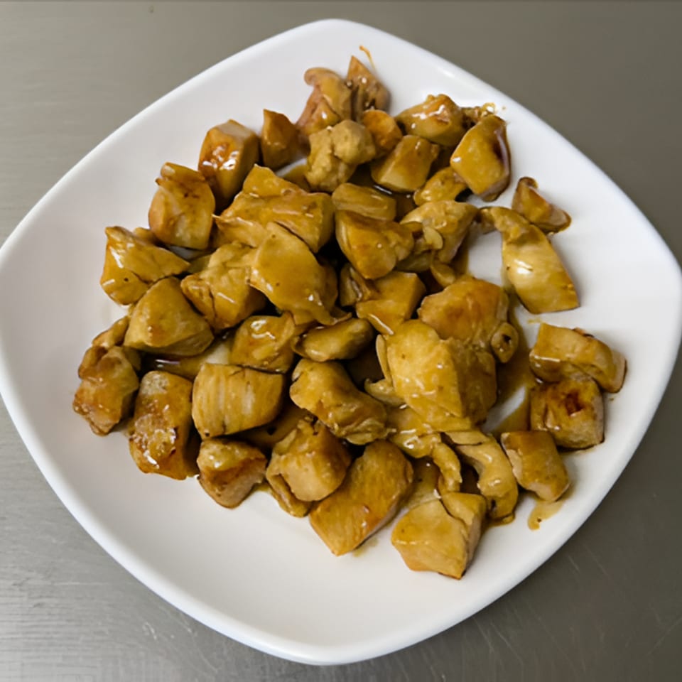Plate of bite-sized golden-brown sautéed chicken pieces served on a white square dish.